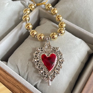 Close-up of a silver sacred heart pendant with red inlay on a gold beaded chain