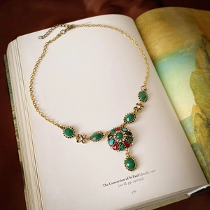 Detail of vintage gold necklace with green gemstones resting on an antique open book