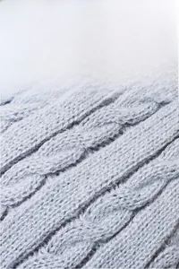 Close-up of thick light gray cable knit fabric showing soft texture and warm insulation