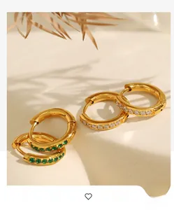 Detail of gold hoop earrings set with green emeralds and white cubic zirconia stones