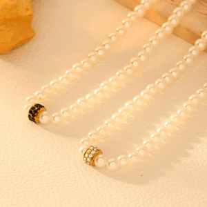 Vintage 18k gold plated pearl necklace with rhinestone cylinder charms on textured surface