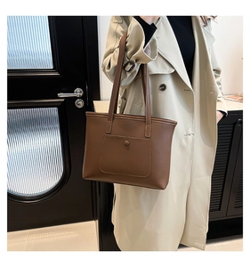 Detail of a brown leather tote bag with a round buckle front pocket and slim shoulder straps