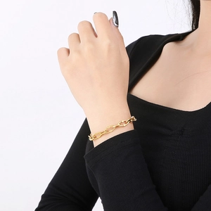 Close-up of a stylish gold lip chain bracelet worn on a model's wrist with a white background