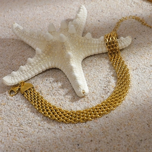 Detail of multi-layer woven mesh gold bracelet with lobster clasp on beach sand