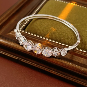 Detail of silver wavy bangle with seven circular zircons on green velvet background