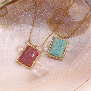 Detail of pink and teal rectangle stone pendants on gold necklaces against shell
