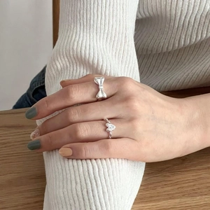 Detail view of 925 sterling silver bow and heart rings worn on finger in a cozy setting