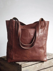 Gros plan du sac cabas vintage en cuir marron avec sangle en tissu sur coffre bois
