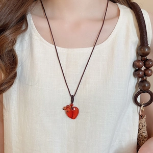 Detail of red stone heart pendant necklace worn on neck with dark brown woven cord