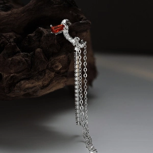 Macro view of silver geometric ear cuff featuring a red gemstone and long fringe chains