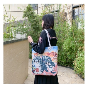 Blue canvas tote bag with cute cartoon cats and white rope handles shown in use