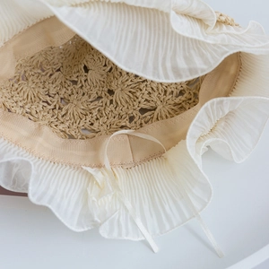 Close-up of handmade straw hat featuring elegant white pleated lace and silk ribbon ties