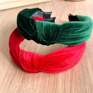 Elegant red and dark green velvet knotted headbands displayed on a light wooden background
