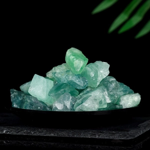 Pile of natural green fluorite rough stones on a dark tray with green leaves background
