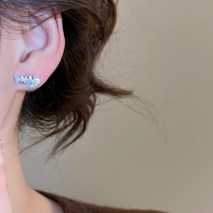 Close-up of polished silver fishbone stud earring worn by model on a grey background