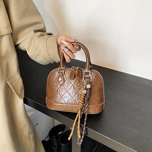 Detail of a brown quilted leather shell bag with bicolor woven handle accessory