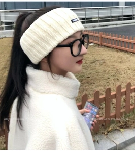 Close-up of a white ribbed knit headband with a minimalist brand label on the front
