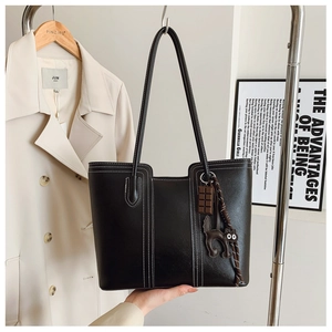 Detail view of a black leather tote bag with white stitching and cute bag charms