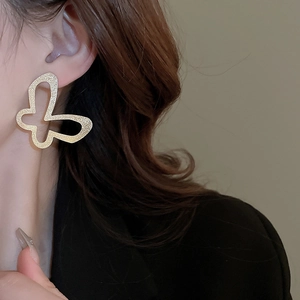 Detail shot of large hollow butterfly earring in matte gold on a model's ear
