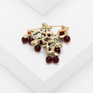 Detailed close-up of a golden leaf brooch with dark red beads on a minimalist background