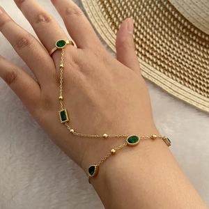 Detailed close-up of a gold hand harness with green emerald zircon stones on a plush surface