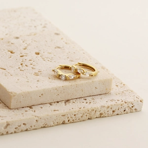 Close-up of gold hoop earrings with marquise-cut cubic zirconia on beige stone