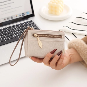Detail of cream-white litchi grain wallet with elegant golden leaf zipper and wrist strap