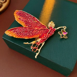 Macro detail of fairy brooch with red enamel wings and a sparkling star pendant