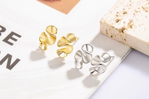 Detailed macro shot of minimalist wavy metallic studs in polished gold and silver finishes