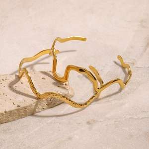 Detail showing two gold wavy open bangles with smooth and hammered textures on stone