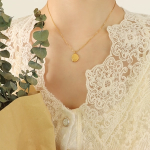 Golden irregular oval pendant necklace in stainless steel worn by a model in lace