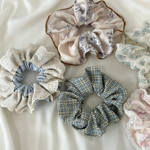 Flat lay of five large lace and silk scrunchies in varied colors on white fabric