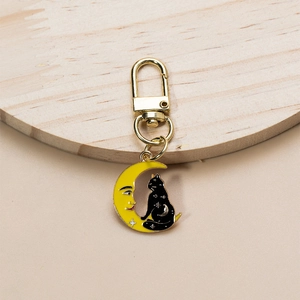 Detail of yellow moon and black cat metal keychain charm with golden spring clasp