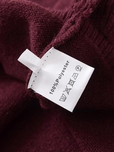 Detail view of wine red knitwear fabric and care label showing 100% polyester composition