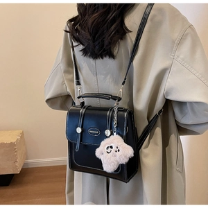 Detail of structured black faux leather backpack with contrast stitching and plush charm