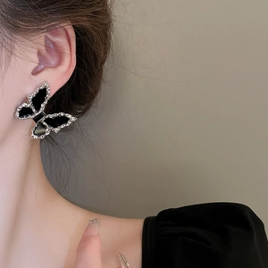 Close-up of elegant black butterfly stud earring with silver trim on a model ear