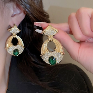 Detailed view of gold earrings with green oval gemstone and pavé rhinestones