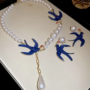 Detailed view of pearl necklace with blue swallow pendant and drop-shaped pearl