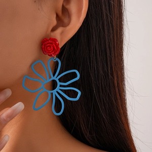Gros plan d'un modèle portant de grandes boucles d'oreilles fleurs ajourées rouge et bleu
