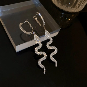 Detailed view of silver snake-shaped long earrings with white rhinestones on black glass