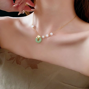 Detail view of gold-plated ginkgo leaf and green donut pendant necklace on model