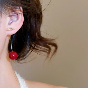 Close-up of elegant deep red resin cherry earrings with golden hooks worn by a model