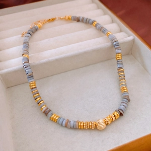 Detail view of striped shell bead necklace with a textured golden sphere pendant on velvet