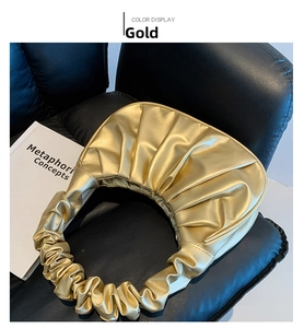 Detail of a golden pleated handbag with metallic finish on a black leather chair