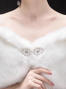 Close-up of a white faux fur bridal shawl with a sparkling rhinestone bow brooch detail