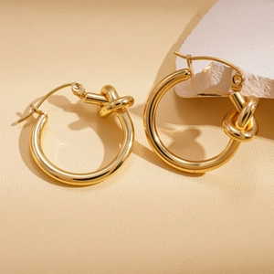 Détail macro de boucles d'oreilles créoles nouées dorées sur support en pierre