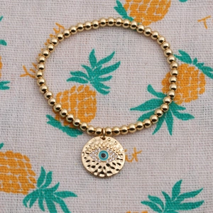 Detail of gold beaded bracelet with blue enamel evil eye charm on pineapple print fabric