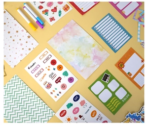 Vista plana de set de papelería colorida con pegatinas y blocs de notas sobre fondo amarillo