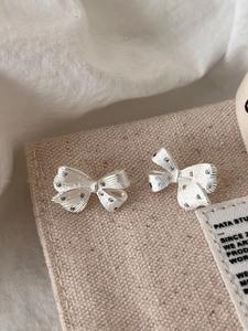 Detailed macro view of silver bow-shaped stud earrings with brushed metallic texture