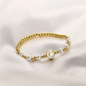 Détail d'un bracelet perlé avec perles dorées, perles blanches et breloque Main de Fatma